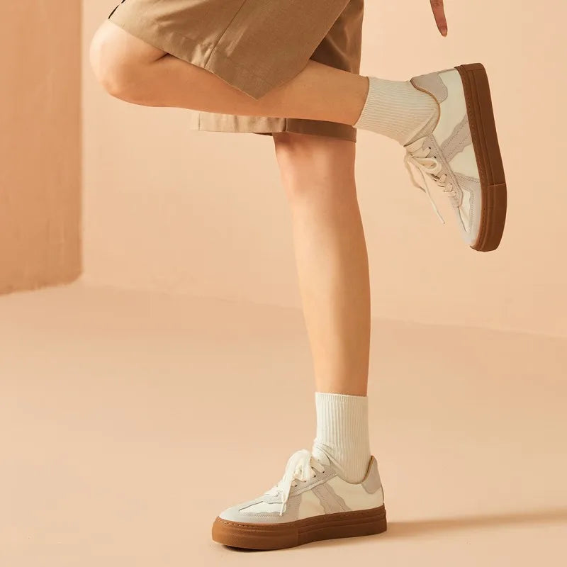 Person wearing white sneakers with brown soles on a beige background