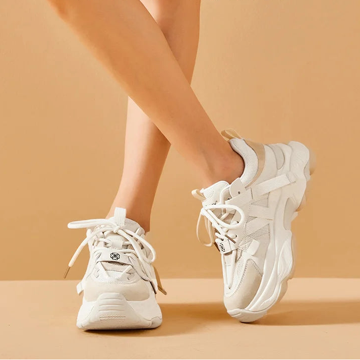 White sneakers worn by a person on a beige background 