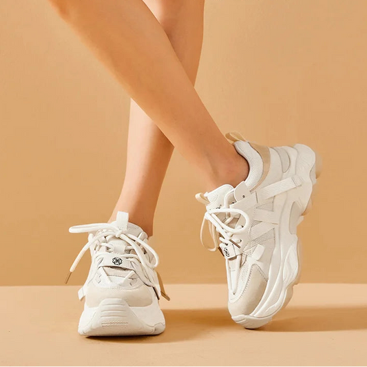 White sneakers worn by a person on a beige background 