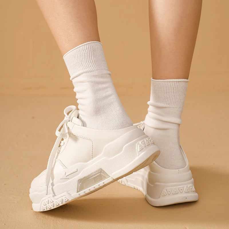 White sneakers worn with white socks on a beige background