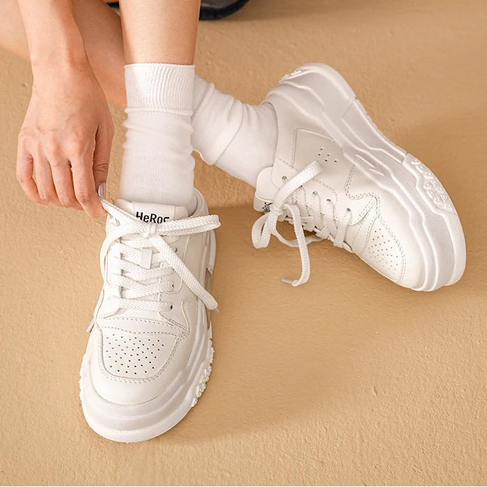 White sneakers being worn on a beige surface 